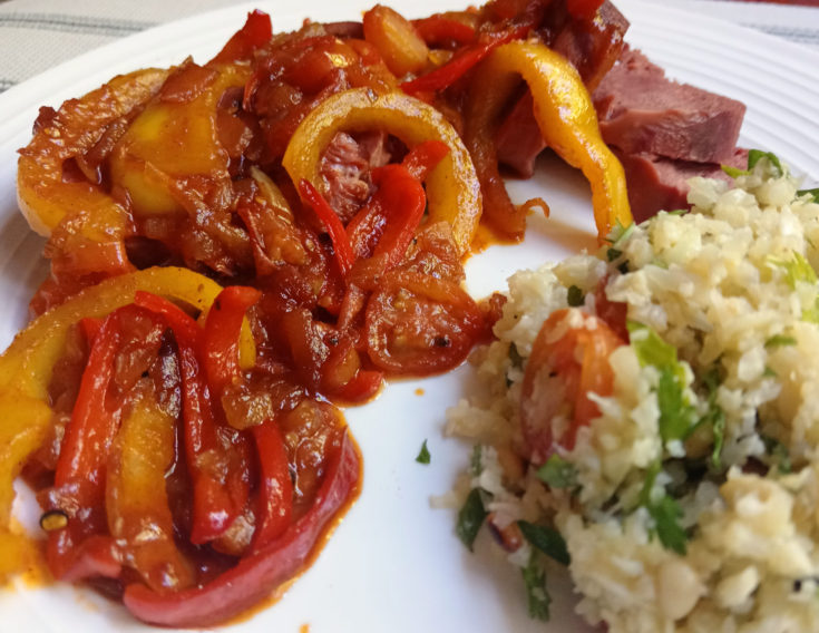 Close-up of sliced beef tongue topped with a glossy bell pepper chutney in shades of red and yellow, served on a white plate with a small portion of cauliflower salad — a warm, colourful keto meal full of balance and natural flavour.