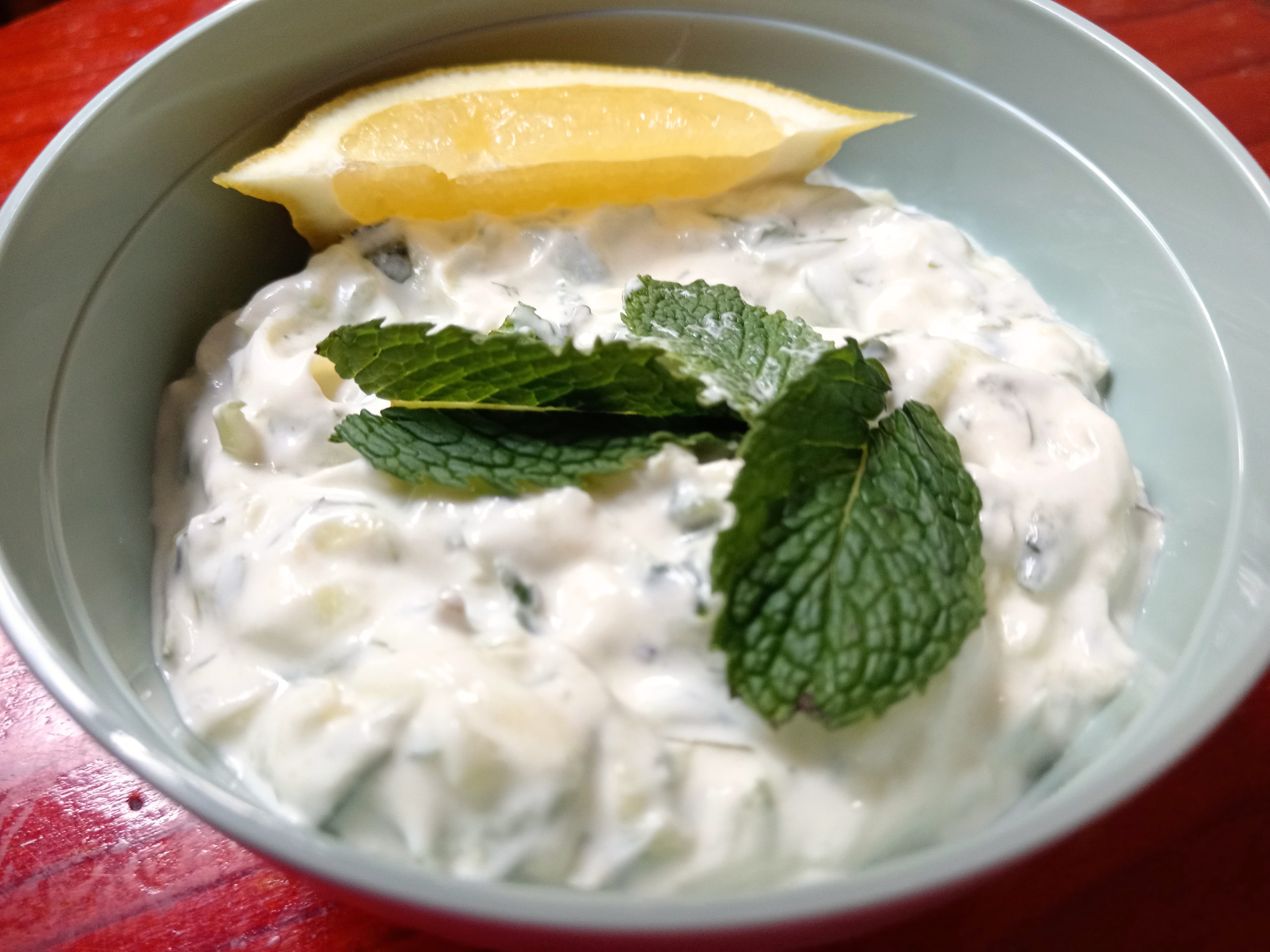 A small bowl of creamy keto tzatziki topped with mint leaves and a lemon wedge, showing its fresh texture and vibrant colour.